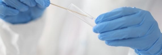 Nous innovons pour vous : le séquençage NGS du SARS-CoV-2 Doctor holds test tube and cotton swab in his hands with medical gloves in laboratory close-up