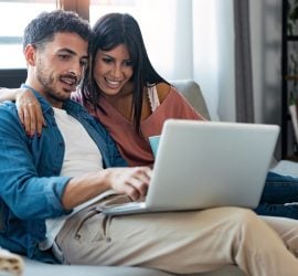 Happy beautiful couple using computer while sitting on the couch