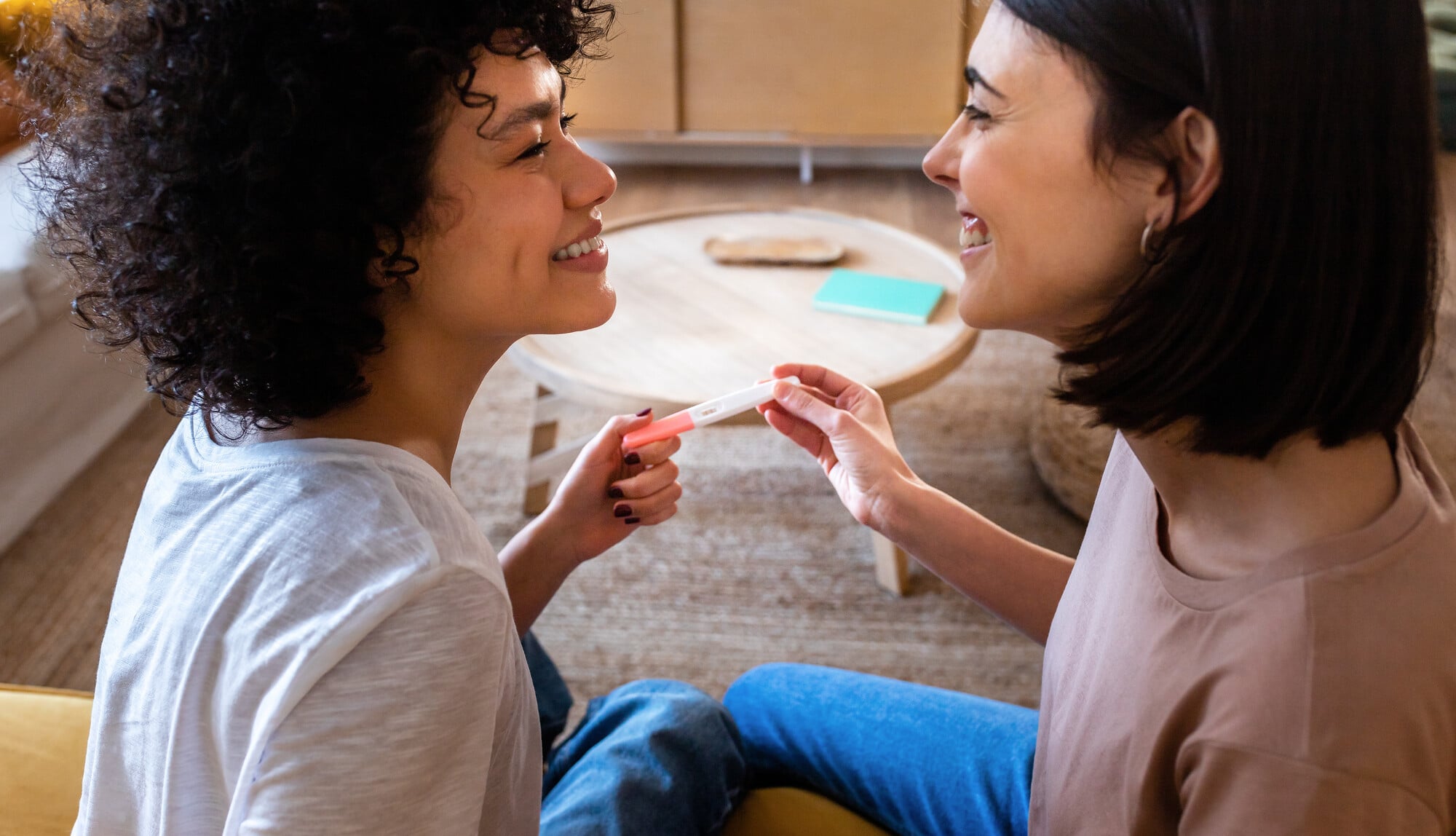 Multiracial lesbian couple in love, looking in the eyes, after finding out positive pregnancy test.